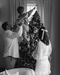 black and white photograph of two people decorating a christmas tree with a baby in the middle