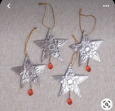 three silver star ornaments hanging from strings on a white cloth covered table with red beads