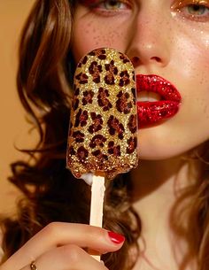 a woman with red and gold glitter on her lips is holding an animal print popsicle