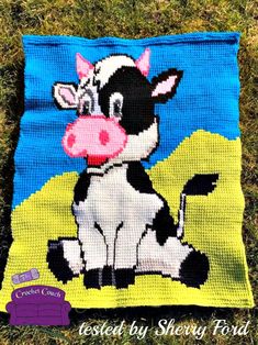 a crocheted blanket with a cow sitting on top of it in the grass