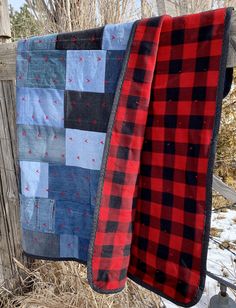 two quilts hanging on a wooden fence in the winter with snow and trees behind them