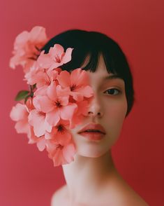 a woman with flowers in her hair is shown from the shoulders down, against a pink background