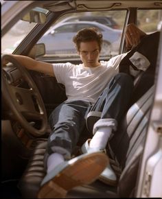 a man sitting in the driver's seat of a car with his foot on the steering wheel