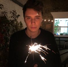 a young man holding a sparkler in his right hand and looking at the camera