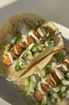 two tacos with chicken, lettuce and cucumber in them on a white plate