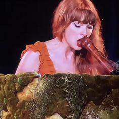 a woman with long red hair is holding a pipe in her mouth as she sings on stage