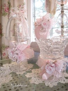 two glass vases sitting on top of a table covered in pink flowers and pearls