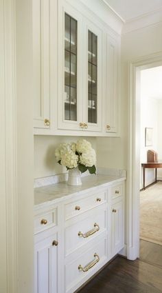 white cabinets with glass doors and flowers in vase on the counter top, along with hardwood flooring