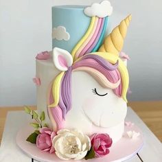 a cake with a unicorn face and flowers on the top is sitting on a table