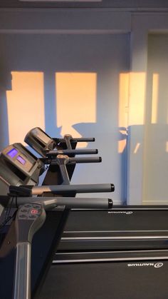 an exercise room with treadmills and cardio machines in the foreground, sunlight shining on the wall