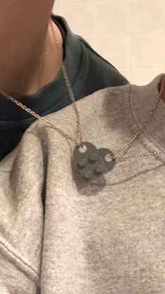 a man wearing a grey sweatshirt with a heart shaped pendant on his neck and two silver circles hanging from it