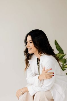 a woman sitting on top of a white chair next to a potted green plant