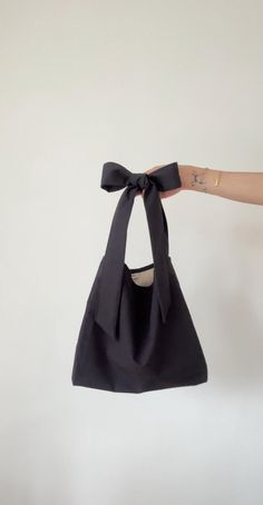 Black shoulder bag with tie-up closure and bow on the shoulder. Adjustable straps. You can wear this bag on your shoulder or as a crossbody bag. You can tie the bow on the shoulder or across your chest. Made from organic vintage cotton. This bag is attributed to its timeless, versatile design. It would look cute with any outfit. It's sustainable and chic, with retro aesthetics. We use our own patterns and designs. We only use non-toxic, longevity organic fabrics to last a lifetime. Most of our f Bow Tote Bag Pattern, Chic Bags With Detachable Bow For Everyday Use, Chic Everyday Bags With Bow Detail, Chic Everyday Bags With Bow, Chic Shoulder Bag With Detachable Bow, Elegant Tote Shoulder Bag With Bow, Elegant Bow Tote Shoulder Bag, Daily Use Tote Bag With Bow, Tote Shoulder Bag With Bow For Shopping