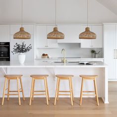 three wooden stools sit in front of an island with white countertops and cabinets