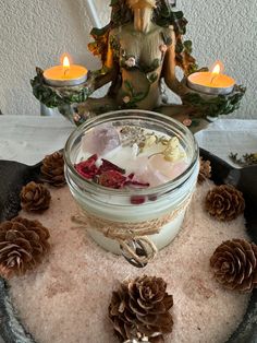 there is a candle and some pine cones on top of a bowl with candles in it