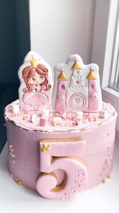 a pink cake decorated with princess figures and gold trimmings on a white table