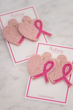 two pink ribbon heart shaped brooches on top of a card with the word therapy