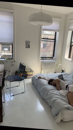 a woman laying on top of a bed in a bedroom next to two large windows