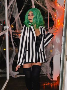 a woman with green hair in a black and white striped suit standing next to a window