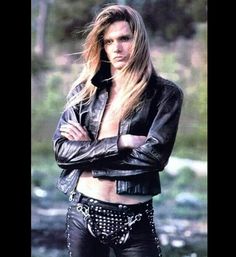 a woman with long hair and leather pants posing for a photo in front of some rocks