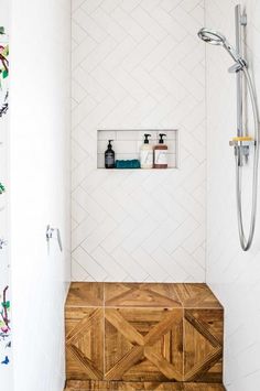 a white tiled shower with wooden bench in the corner and shelves on the wall above it