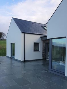 a white house with black slate flooring next to a green field and blue sky