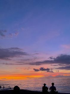 people sitting on the beach watching the sunset