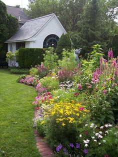 a garden filled with lots of flowers next to a white house and green grass covered yard