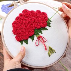 a person holding a red rose in front of a white embroidery hoop