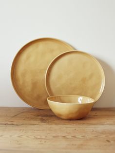 two yellow plates sitting on top of a wooden table next to a bowl and plate