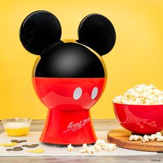 a bowl of popcorn and a mickey mouse head on a wooden table with yellow background