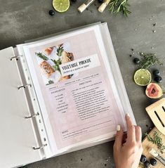 a recipe book is open on a table with fresh fruits and vegetables around it, including figs