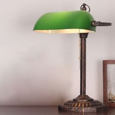 a green lamp sitting on top of a wooden table next to a framed photograph and an old frame