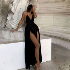 a woman in a black dress leaning against a statue