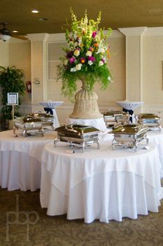 a table topped with lots of food covered in white cloths and flower centerpieces