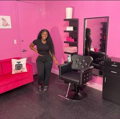 a woman standing next to a chair in a room with pink walls and black furniture