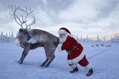 a man dressed as santa claus standing next to a reindeer in the middle of a snow covered field