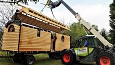 a man standing on top of a tractor next to a wooden structure with a ladder