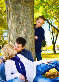 a man, woman and child sitting on the ground in front of a large tree