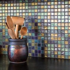 wooden utensils in a ceramic container on a counter top with colorful tiles behind it