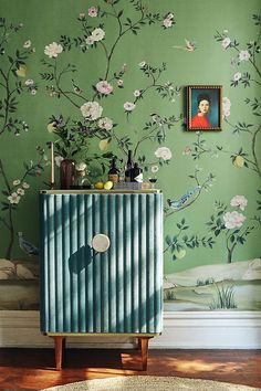 a green room with flowers and paintings on the wall, along with a blue cabinet