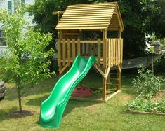 a green slide in the grass next to a wooden structure with a roof on top