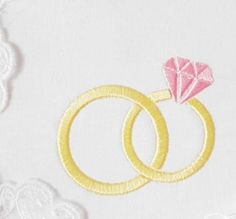 two gold wedding rings with a pink diamond on the middle and white lace around them