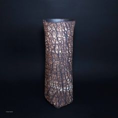 a brown vase sitting on top of a black table next to a dark wall and floor