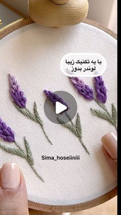 someone is stitching purple flowers on a white piece of fabric with a wooden frame