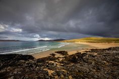 the beach is covered in rocks and water under a cloudy sky with mountains in the distance