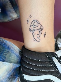 a small mushroom tattoo on the foot of a person's leg, with stars around it