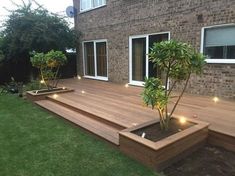 a wooden deck with planters and lights in the grass next to a brick building