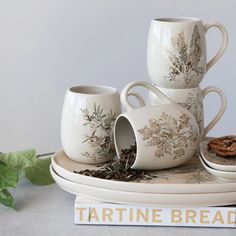 a stack of coffee cups sitting on top of a plate next to cookies and leaves