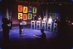 people are sitting on the stage in front of microphones with game show written on them